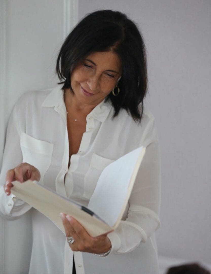 A woman in white shirt holding open book.